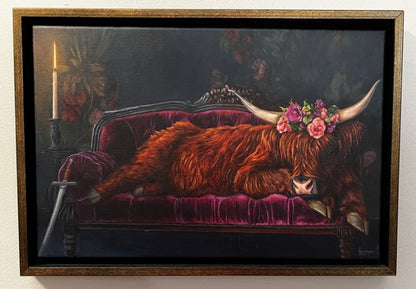 Framed artwork of a cow with flowers on a velvet couch against a dark background.